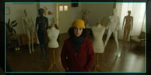On-set monitor frame from Shahid: a woman in a yellow beanie and red coat stands center in a room filled with dressmaker mannequins and full-body forms, daylight filtering through curtains; camera HUD with “FPS 25, 5600K” surrounds the image.