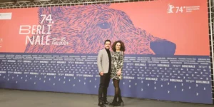Red carpet photo at the 74th Berlinale: two guests, Baharak Abdolifard and Nima Nazarinia, pose in front of a large bear-graphic backdrop reading “74. BERLINALE — 15–25 Feb 2024,” with festival branding across the step-and-repeat.