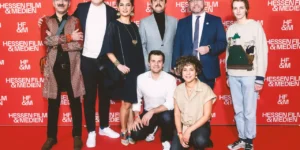 Red carpet photo for Shahid: eight attendees pose against a red “Hessen Film & Medien” step-and-repeat—six standing, two kneeling at front.